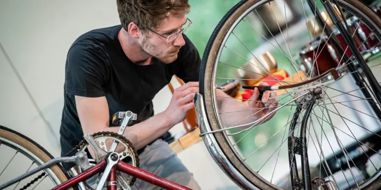 Ein junger Mann spielt Musik mit einem Geigenbogen auf einer Fahrradspeiche